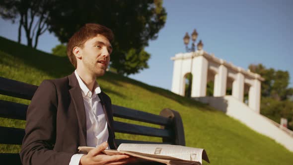 Slow Motion Handsome Businessman Manager Ceo in Suit Reading Morning Newspaper on Bench in Green