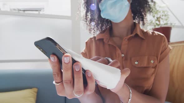 Woman wearing face mask wiping her smartphone with a tissue