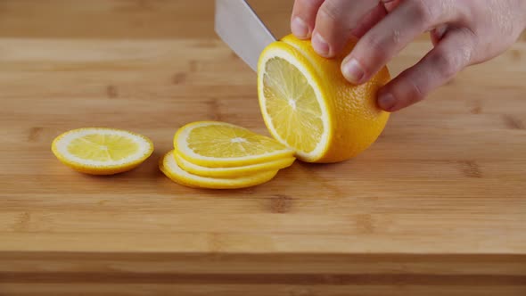 Hands Slicing A Piece Of Juicy Lemon On The Wooden Chopping Board With A Sharp Knife - close up