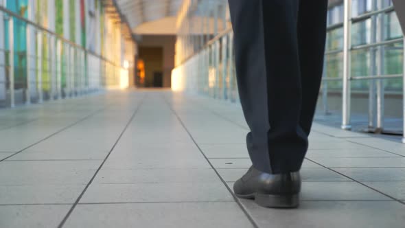 Feet of Successful Businessman Walking in Hall of Terminal and Pulling Suitcase on Wheels. Legs Of