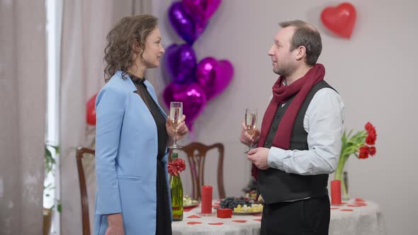 Side View of Happy Loving Adult Couple Standing with Champagne Glasses Talking