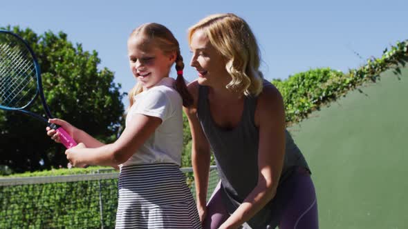 Caucasian mother teaching her daughter to play tennis at tennis court on a bright sunny day