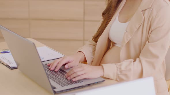 Pregnant business woman sitting and working on the laptop with sale report