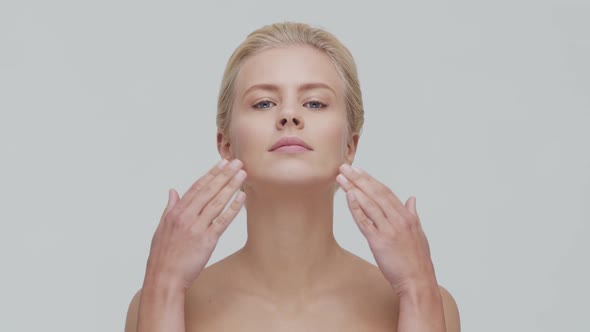 Studio portrait of young, beautiful and natural blond woman applying skin care cream. F