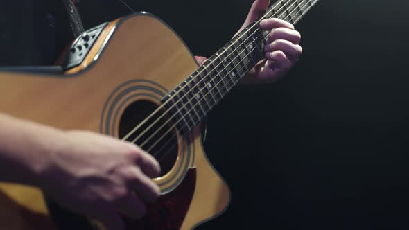 Close-up of a guitarist playing chords on an acoustic guitar in a dark room.