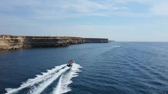 Fast Boat with People Sails Along the Rocky Coast in the Summer