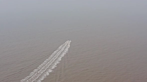 Aerial drone shot towards a speed boat on muddy water hazy day