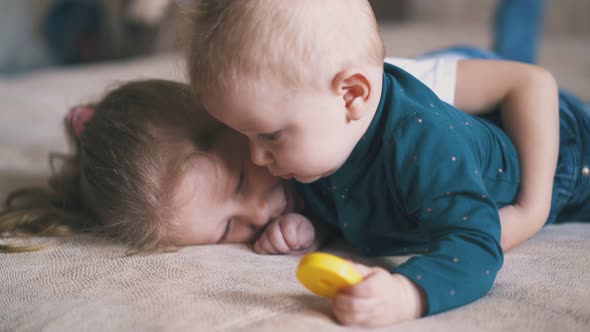 Girl Swings Legs Hugging Brother with Yellow Toy on Bed