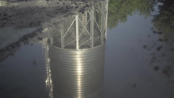 Camera Moves Down Along Reflection of Huge Reservoir in Clear Paddle. Large Cement Storage Silo