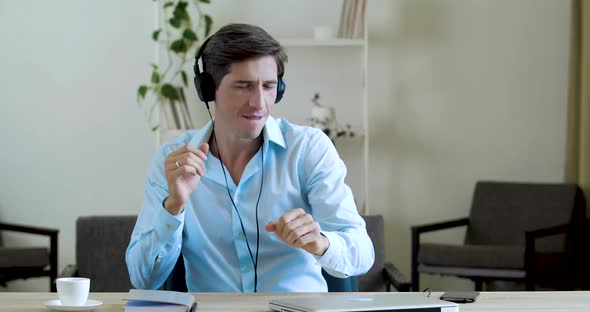 Happy Businessman Relaxing in Office at Desk Listening Music in Wireless Headphones, Moving Arms As