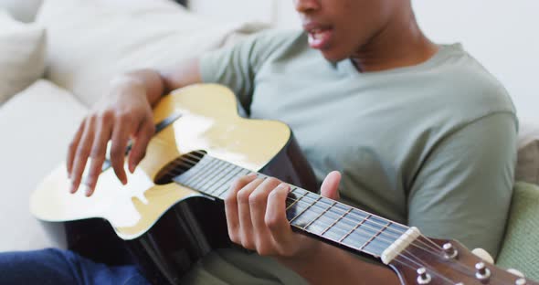 Happy african american man plays guitar and singing at home