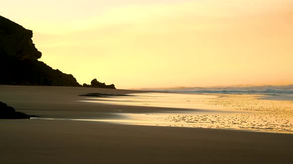 Soft golden light during sunrise over pristine beach, wet sand reflection