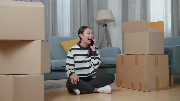 Asian Woman With Cardboard Boxes Talking On Smartphone After Moving Into A New House 