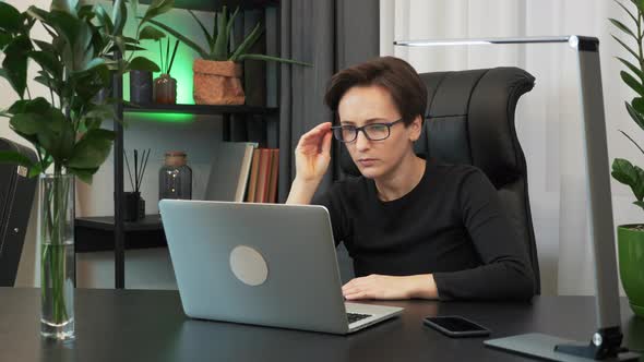 Overworked businesswoman is sitting at workplace desk and using laptop computer