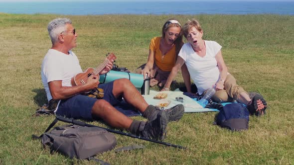 Adult family playing ukulele and singing sitting on a blanket during an excursion