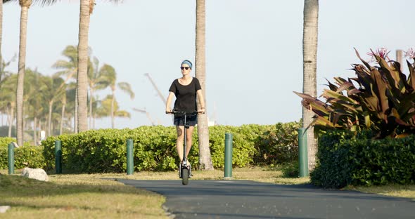 Young Woman Riding Electric Scooter in Tropical Park on Sunny Evening Full Frame