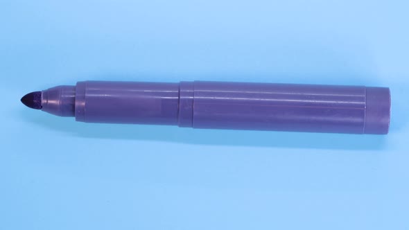 Purple marker pen rotating on blue surface background, macro shot close up view detail.