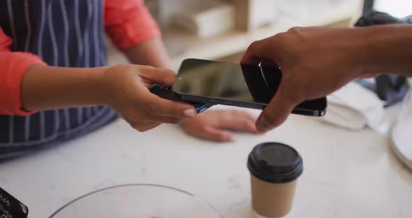 Video of hands of biracial man paying with smartphone for coffee