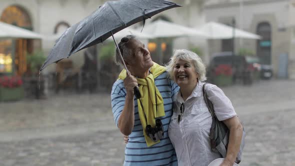 Happy Senior Tourists Stand Downtown and Enjoy the Rainy Weather in Lviv