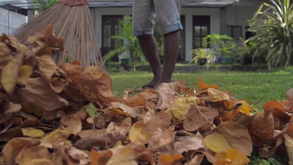 Young Man in Flip Flops Holds Broom and Cleans Leaves