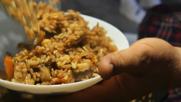 a Person Puts a Skimmer Into a White Bowl a Portion of Cooked Hot Uzbek Pilaf From Which Steam and