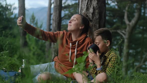 Mother with son making video call by phone while relaxing in the forest