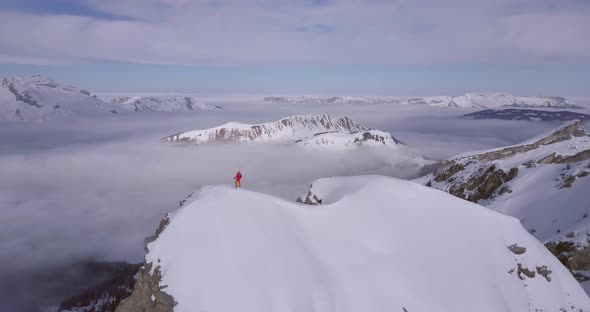 Aerial drone view of a mountain climber skier on the peak summit top of a snow covered mountain