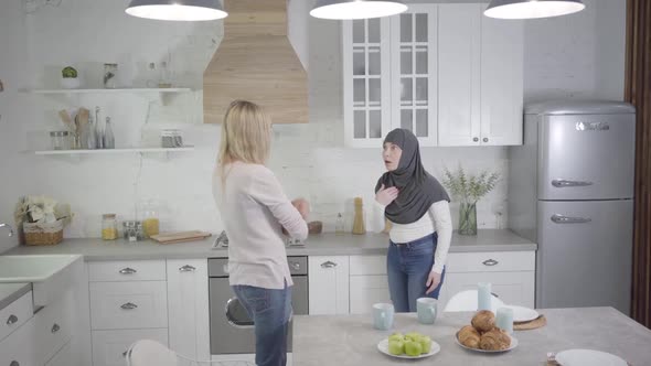 Adult Caucasian and Muslim Woman Arguing at Home, Lady in Hijab Turning Back To Friend. Two Friends