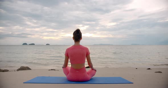 Back Shot Woman Sitting the Beach on Yoga Mat She is Meditating in Lotus Pose Against the Sunset