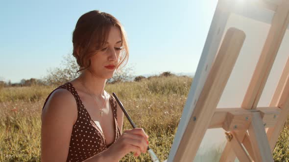 Close-up concentrated girl painting on canvas outdoors