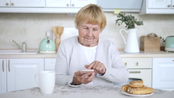 Portrait Of Happy Senior Woman Using Smartphone At Home Kitchen.