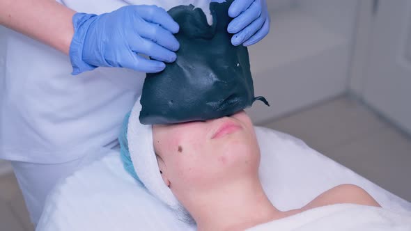 Cosmetologist Removing Alginate Mask From Young Woman