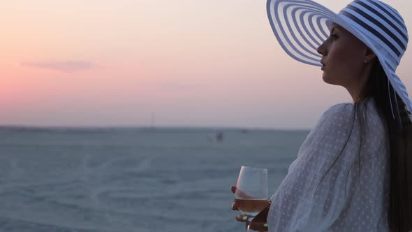 Elegant Woman with Glass of Wine Resting on Beach at Sunset