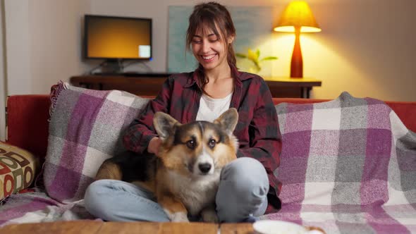 Happy Couple with Cute Pet Welsh Corgi Dog Sitting on Couch at Home at Evening