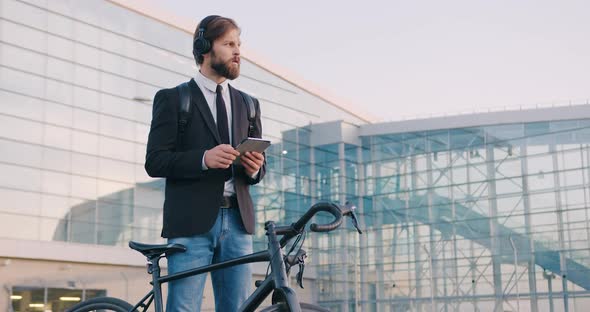 Man in Earphones which Standing Near His Bike and Using Tablet PC