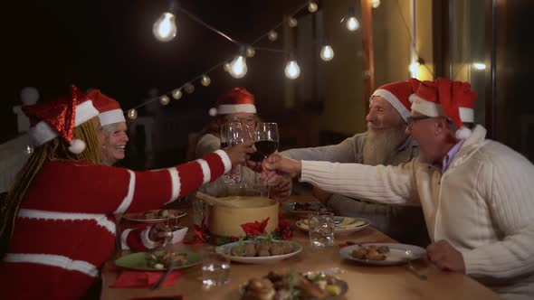 Happy senior friends toasting and celebrating Christmas holidays with red wine glasses