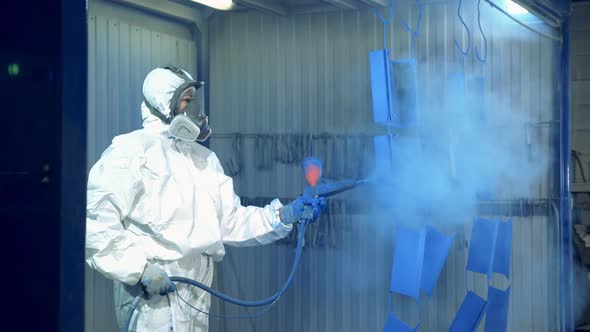 A Worker Is Spraying Blue Paint Onto Metal Pieces at a Painting Factory Facility