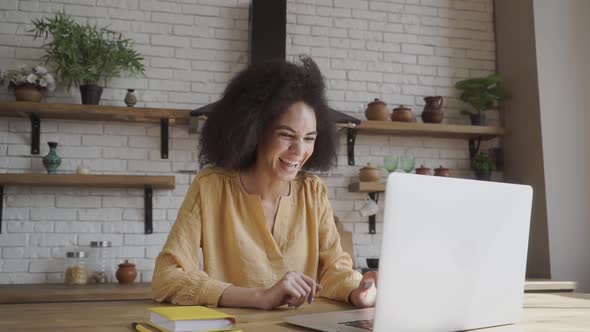 Overjoyed African American Millennial Girl Sit at Desk Laugh Watching Funny Video on Laptop Online