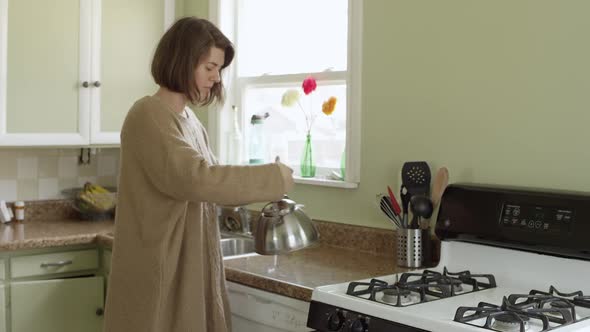 Woman filling tea pot and putting on stove