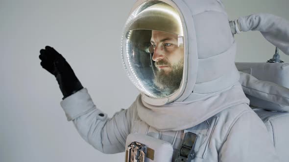 Astronaut Stands with on a Light Background and Waves His Hand