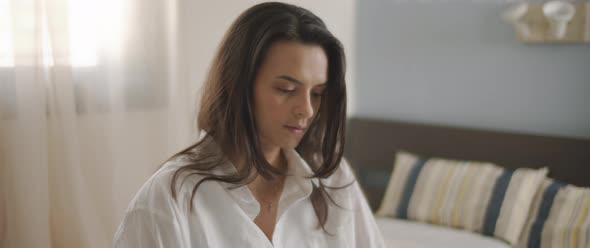 A close up of a young woman in white shirt working from home in her bedroom.