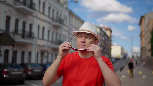 Young Man in a Hat Walks Along the City Street Puts on Sunglasses Camera Movement