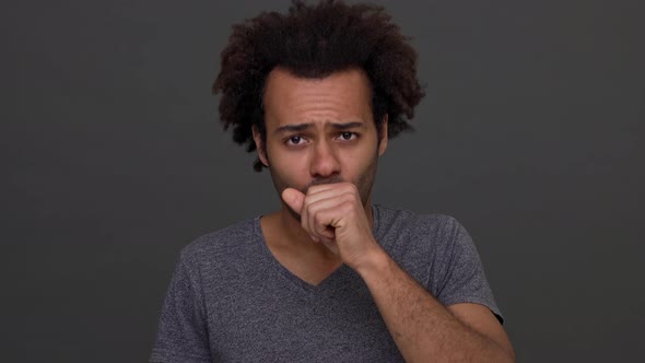 Dark Skinned Man with Afro Haircut Coughing Isolated Over Charcoal Background Laughing Afterwards