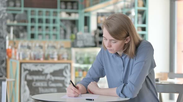 Beautiful Young Woman Writing on Paper in Cafe