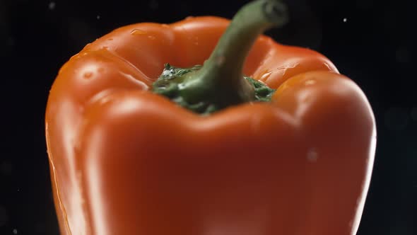 Camera follows water splash on an orange pepper. Slow Motion.