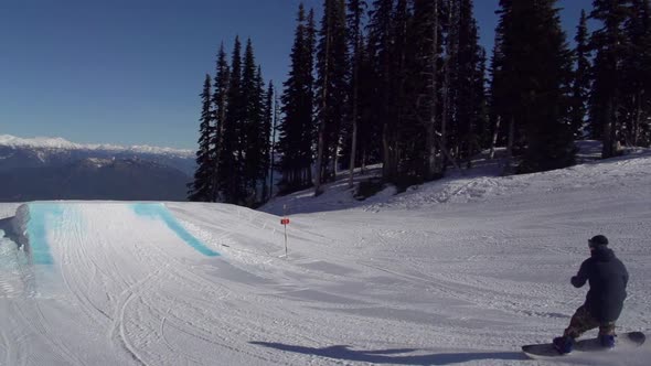 A young man snowboarder going off jumps in a terrain park.