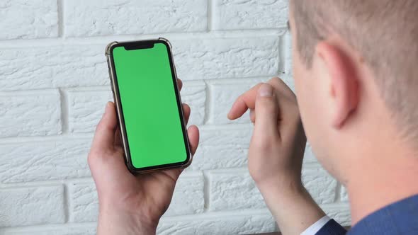 Man Using Smart Phone in Office Space Sitting on Chair and Using Green Screen Phone Mockup Chroma