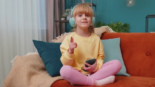 Child Girl Kid with Smartphone in Headphones Dancing Singing Listening Music at Home Alone on Sofa