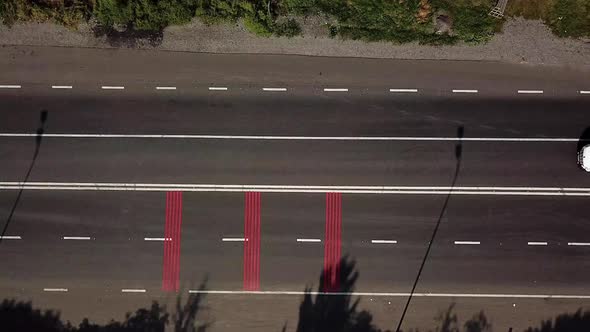 cars are passing on the road with red markings and with a pedestrian crossing. Aerial view.
