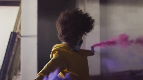 Mixed race woman holding blue and purple flares dancing in an empty building